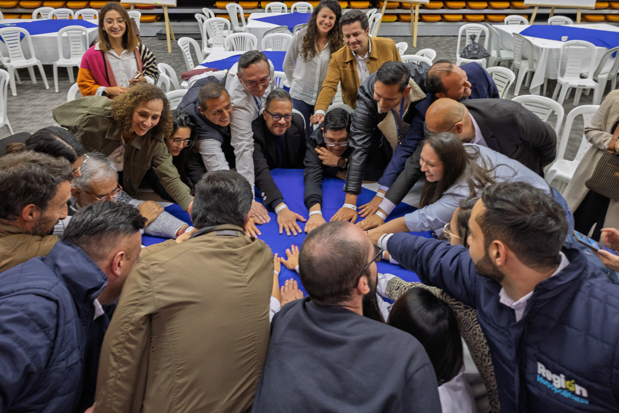 Fotografía de un grupo de personas reunidas en círculo con las manos puestas sobre una mesa en señal de trabajo en equipo al finalizar la mesa temática sobre seguridad alimentaria