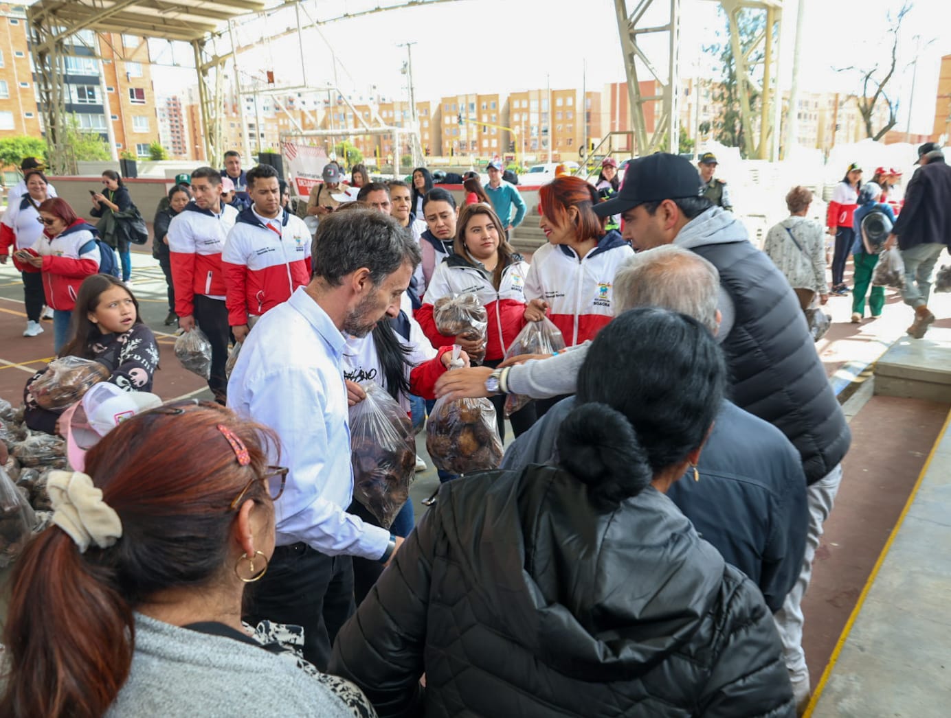 fotografía de la entrega de papa a personas en condición de vulnerabilidad, aparecen el director de la Región Metropolitana y el alcalde Soacha haciendo la entrega, hay personas a su alrededor, en el coliseo deportivo del municipio de Soacha