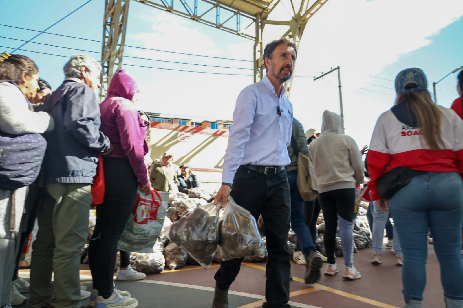 fotografía del director de la región metropolitana bogotá cundinamarca caminando y cargando una bolsa de papa en el coliseo deportivo de Soacha donde se realizó una entrega de papa a comunidades vulnerables