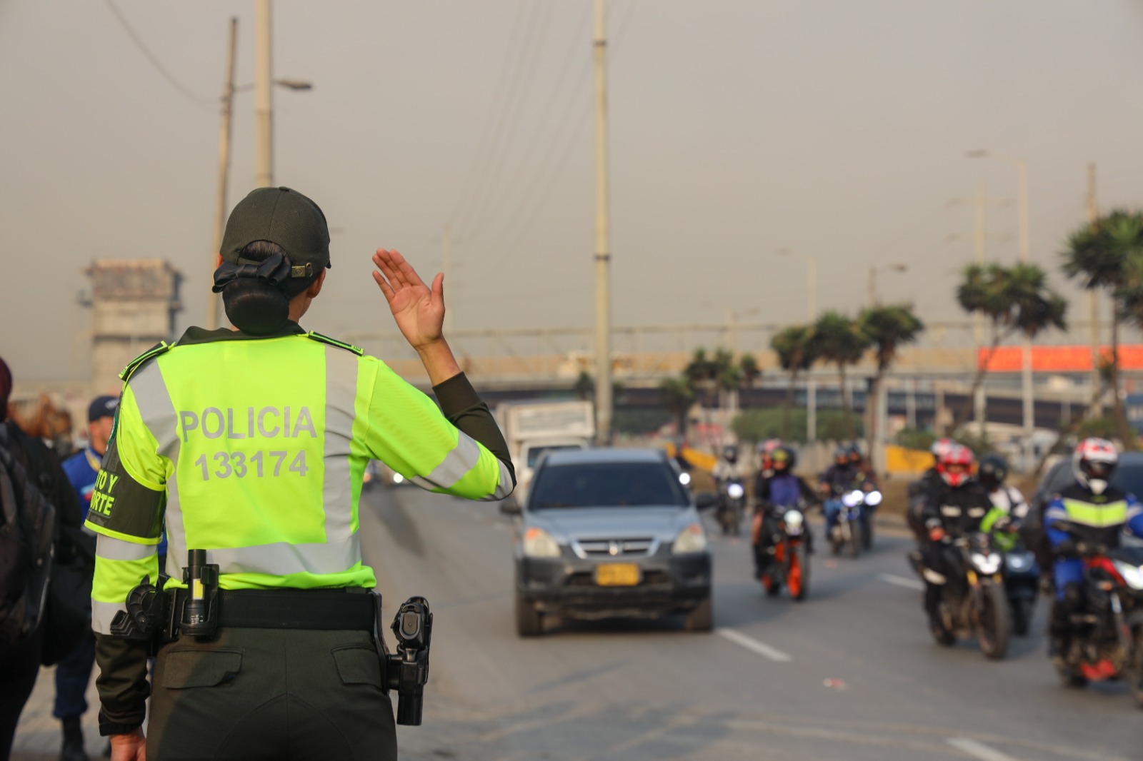 Fotografía de una mujer policía que está de espalda haciendo control del tránsito en una avenida