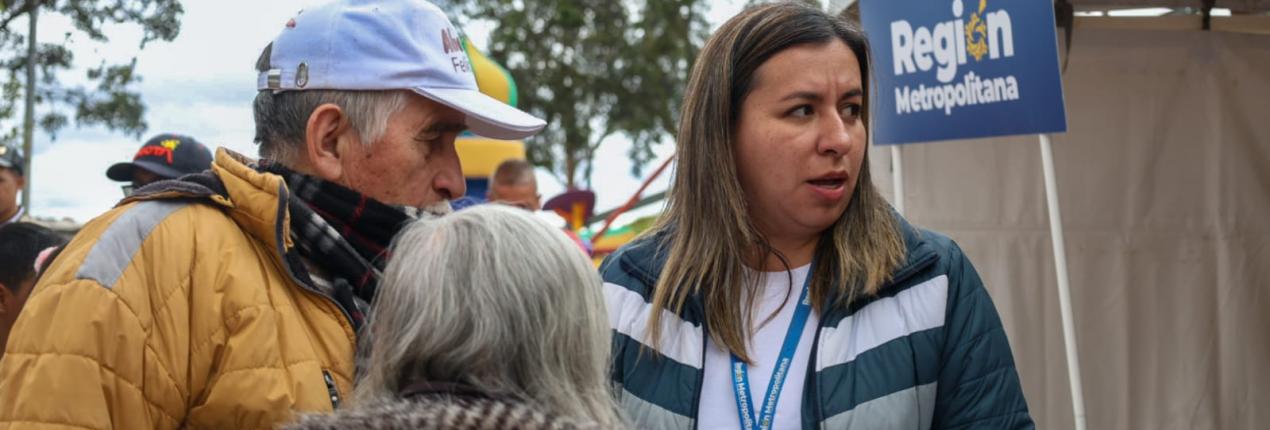 Fotografía de una funcionaria de la región metropolitana atendiendo a una ciudadana alrededor de una carpa instalada en la jornada de atención a la ciudadanía en el borde Bogotá - Soacha