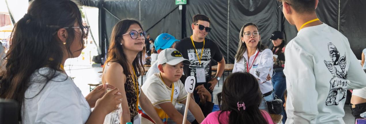 Fotografía muestra a un grupo de niñas, niños y adolescentes en una actividad lúdica alrededor de una mesa ubicada al interior de una carpa grande