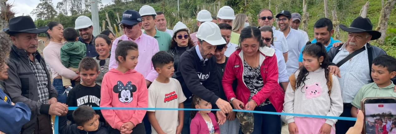Fotografía muestra a un grupo, integrado por niñas, niños y adolescentes y adultos, que participan en el corte de una cinta, durante la inauguración de una placa huella