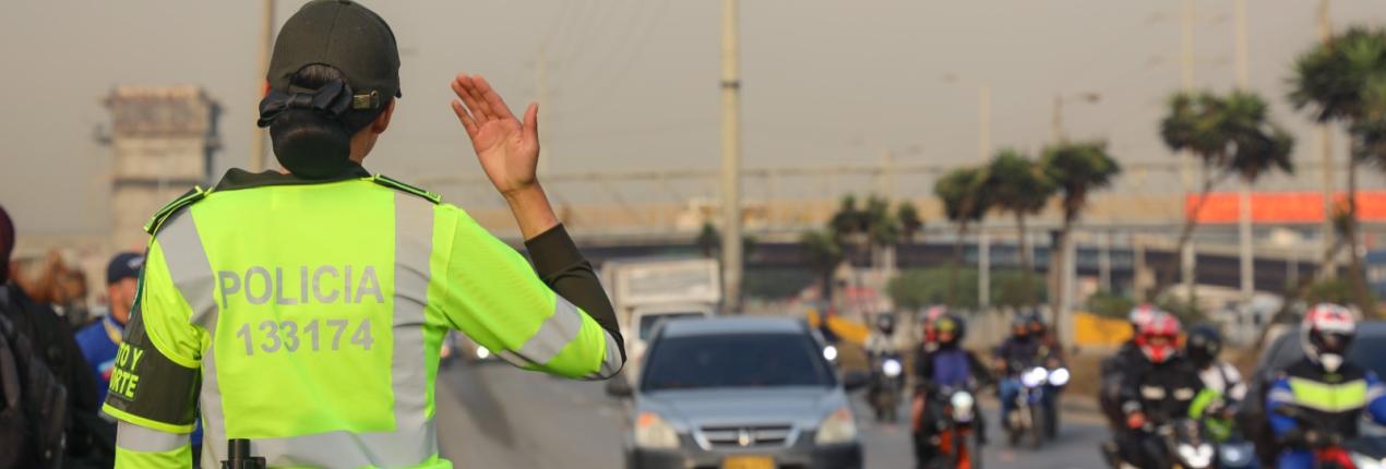 Fotografía de una mujer policía que está de espalda haciendo control del tránsito en una avenida