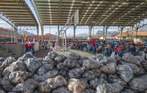 Fotografía de bultos de papas en un coliseo, en el segundo plano, aparecen muchas personas