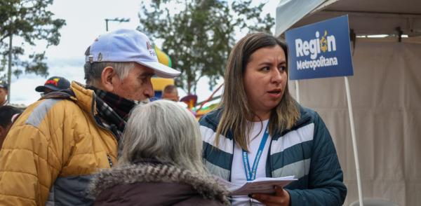 Fotografía de una funcionaria de la región metropolitana atendiendo a una ciudadana alrededor de una carpa instalada en la jornada de atención a la ciudadanía en el borde Bogotá - Soacha