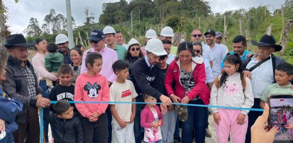 Fotografía muestra a un grupo, integrado por niñas, niños y adolescentes y adultos, que participan en el corte de una cinta, durante la inauguración de una placa huella