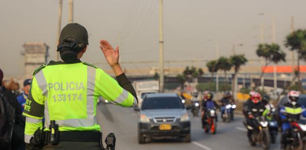 Fotografía de una mujer policía que está de espalda haciendo control del tránsito en una avenida